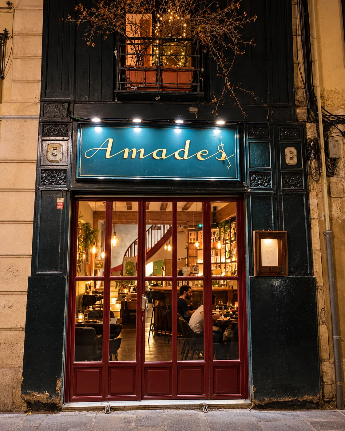 Fachada de Amades con el rótulo azul y la puerta de madera roja, de noche
