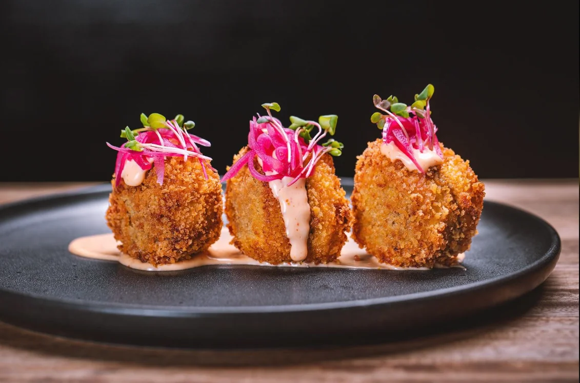 Tres croquetas crujientes con salsa y brotes frescos