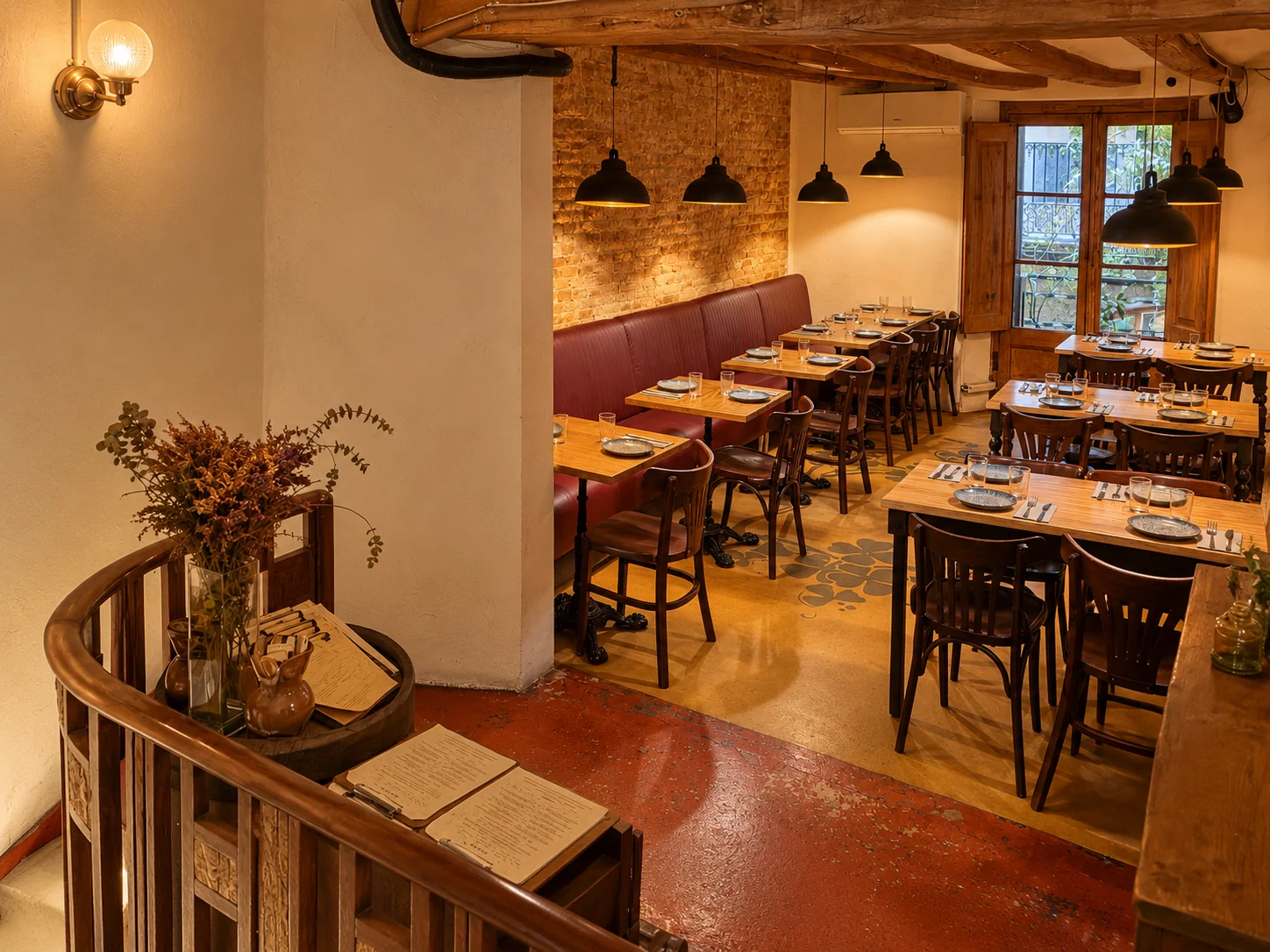 Comedor con pared de ladrillo visto, banco tapizado en rojo, mesas de madera y lámparas colgantes negras